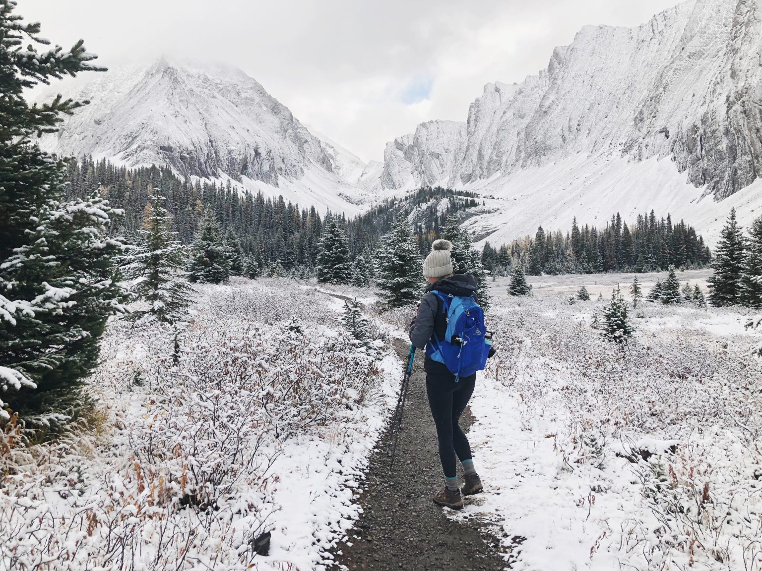 A woman walks a snowy path next to a mountain