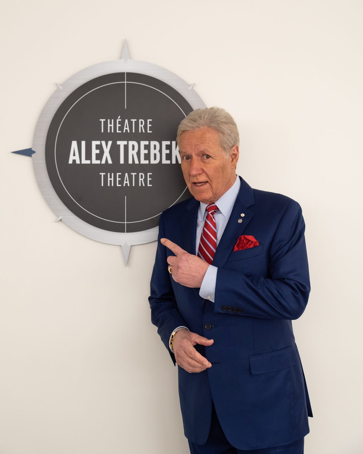 Alex Trebek stands next to a sign that reads 