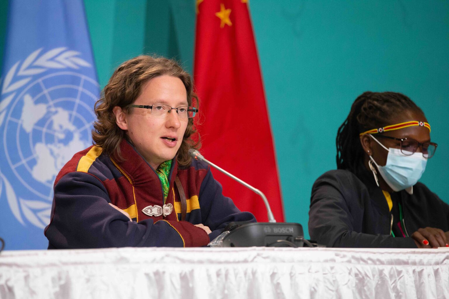 Aslak Holmberg, who is Sámi, speaks on a panel with flags in the background.