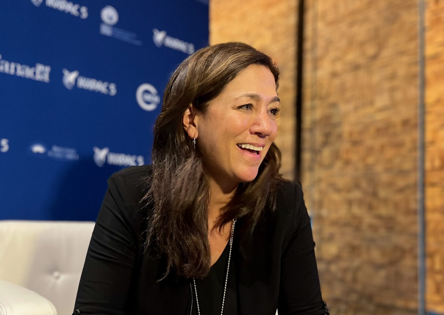A woman with long dark hair laughs with a twinkle in her eye, against a background of blue and wooden accents.