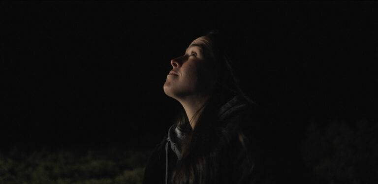 An upturned face, surrounded by darkness, gazes up into the night sky.