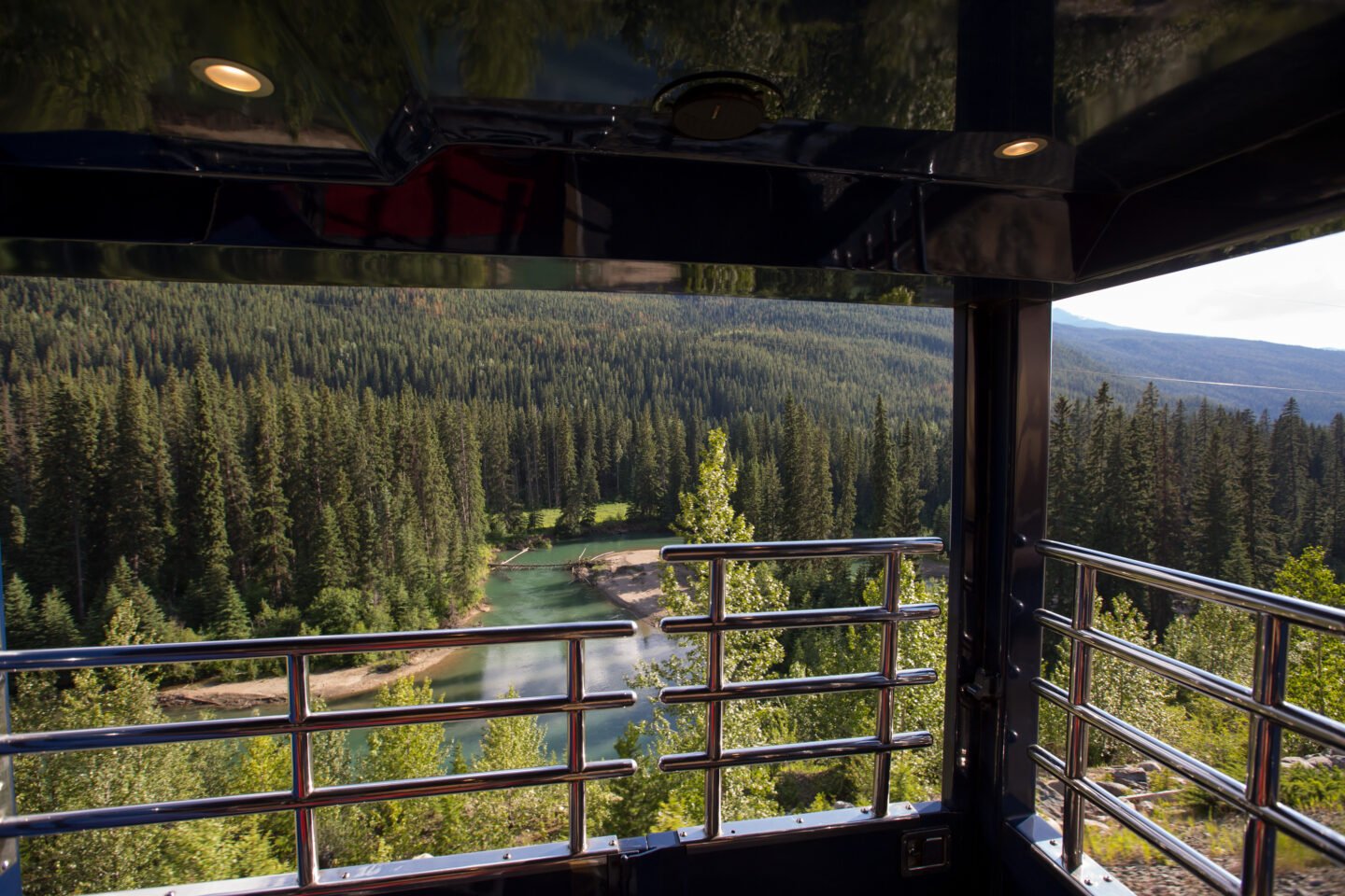 A view of a turquoise river in the Rocky Mountains from a observation deck on a train