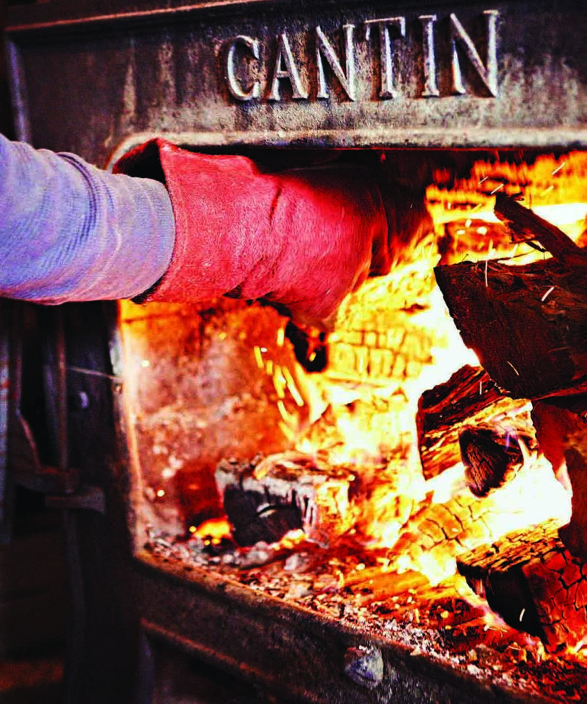 A gloved-hand stokes a fire in a wood stove.