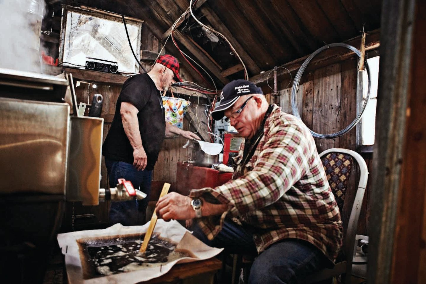 Two men prepare maple syrup at a sugar shack.