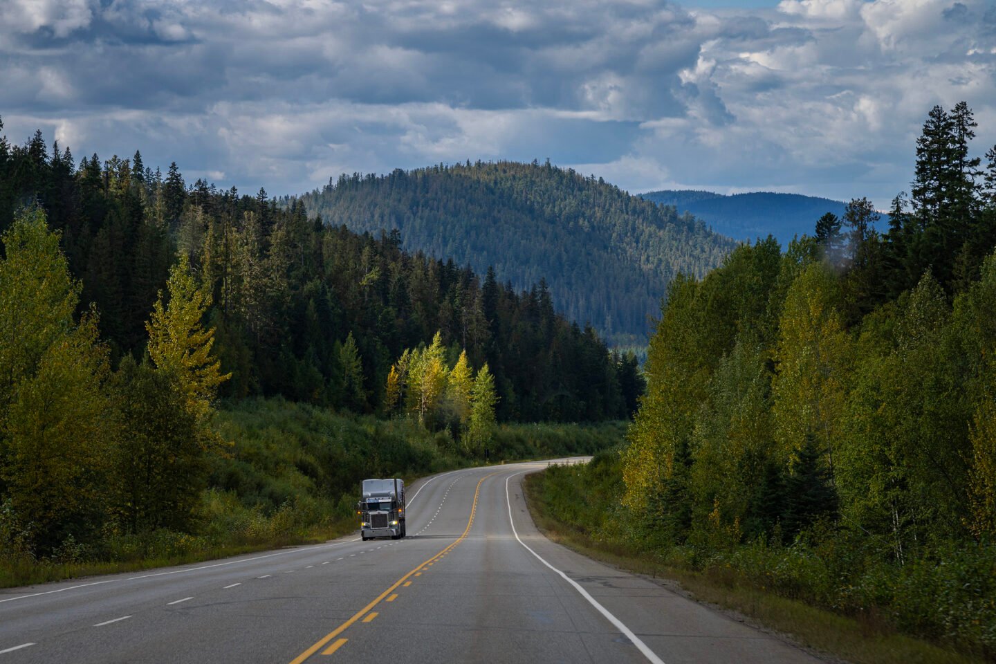 A truck drives down a highway with the rocky mountains in the background