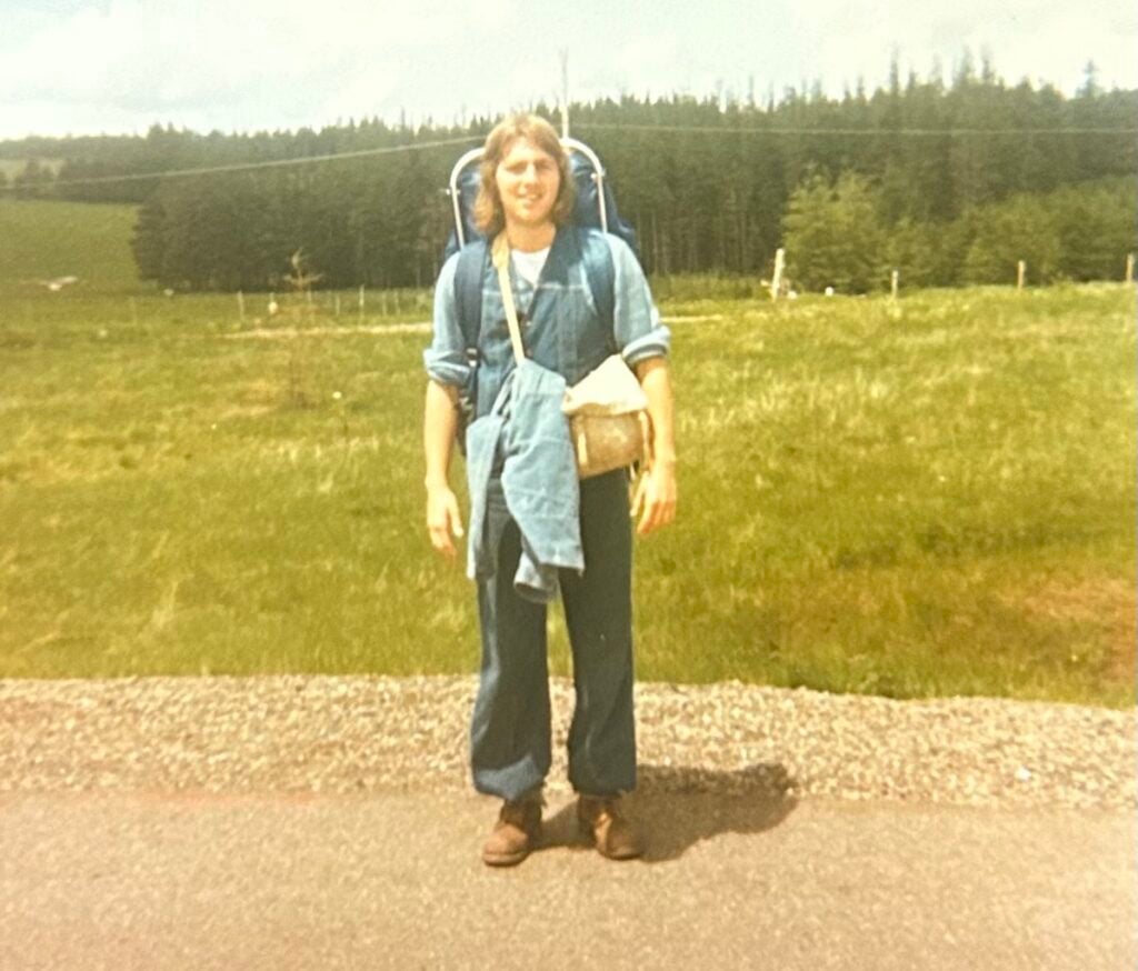 A hitchhiker stands on the side of a Canadian highway in the summer of 1977