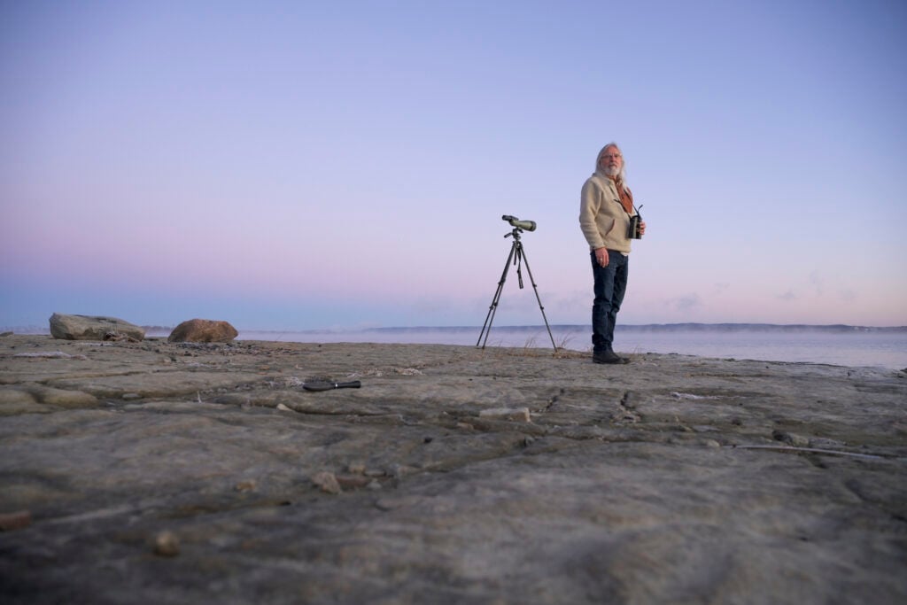 A man stands at the edge of a lake during sunset