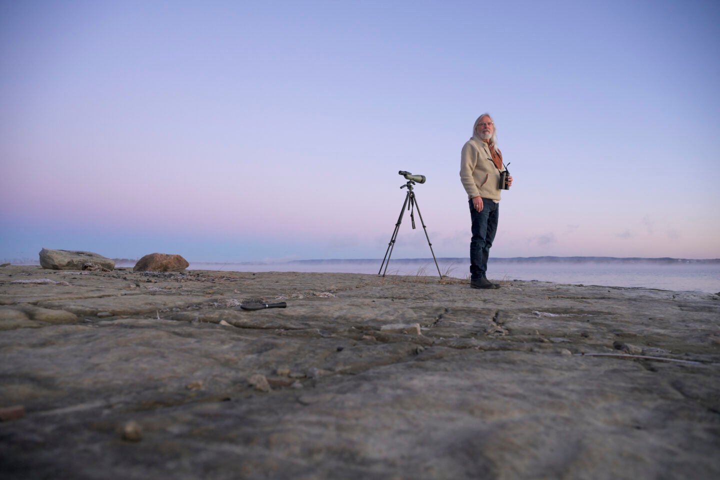 A man stands at the edge of a lake during sunset