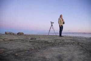 A man stands at the edge of a lake during sunset