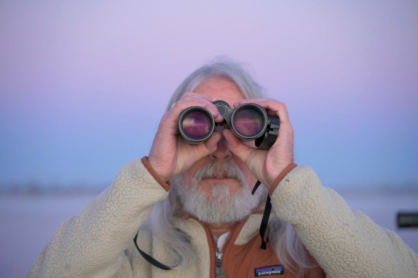 A man looks through binoculars at sunset