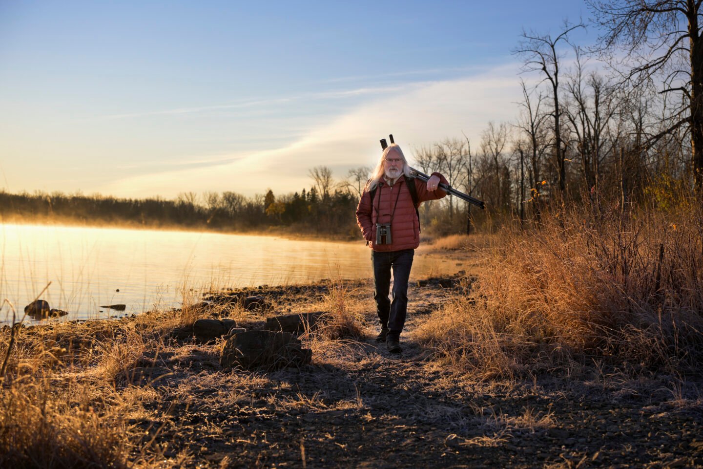 A man carries a tripod on the edge of a lake in the fall