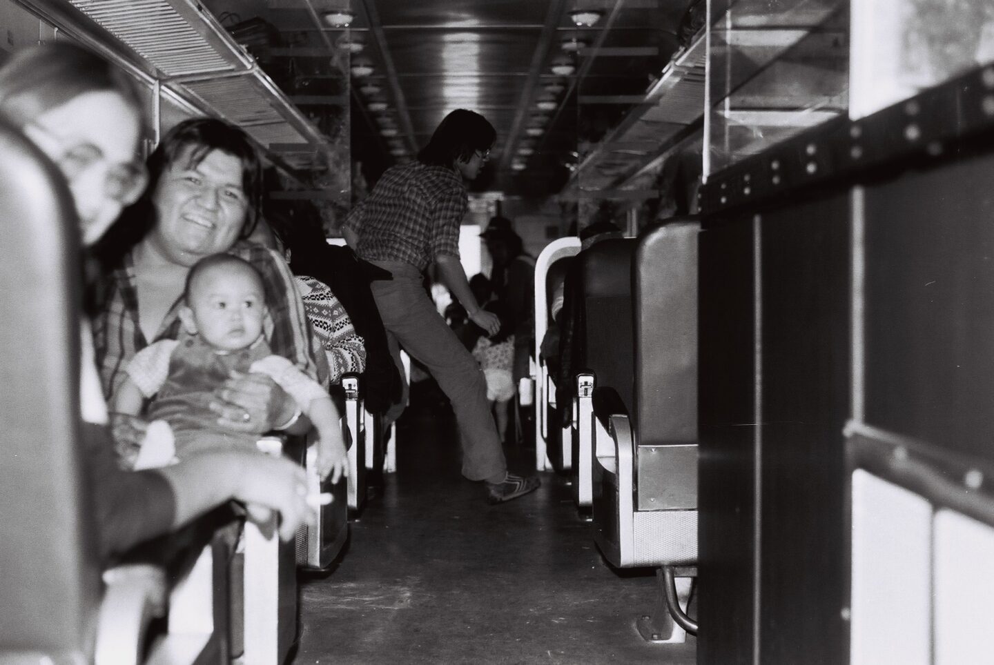passengers in a rail car. one man is holding a baby. the photo is black and white.