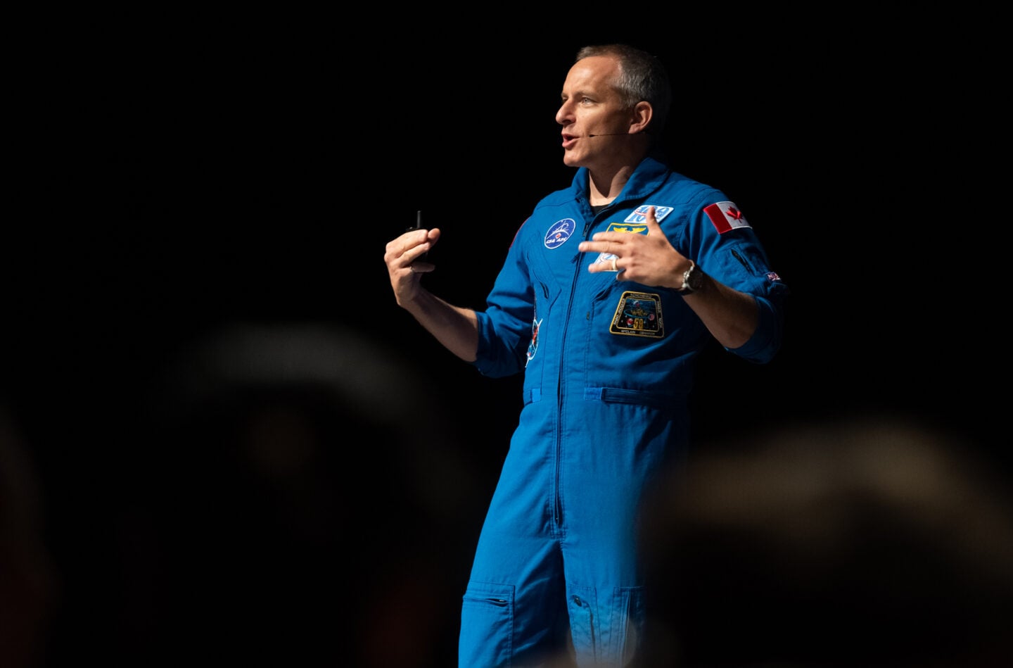 Astronaut David Saint-Jacques speaks in a dark room while wearing a blue CSA uniform.