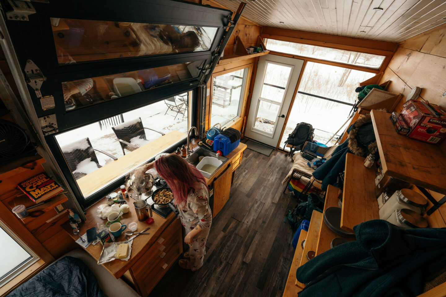 A top down view shows a woman cooking in her pyjamas in a small but neat cabin.