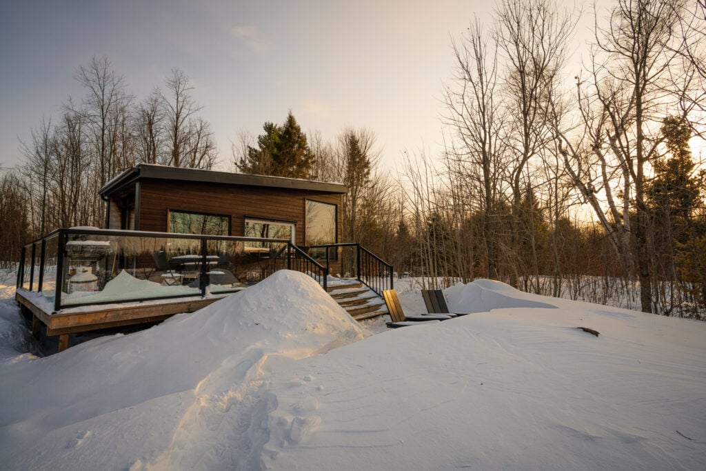 a wooden cabin surrounded by snow and trees at sunset