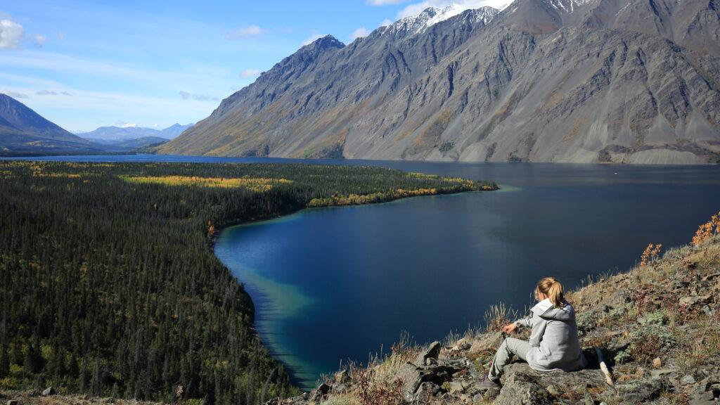 A girl sits on the side of a moutain looking out across a large lake.