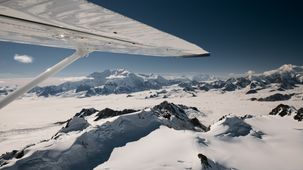 A snow covered mountain is visible from the window of a plane.