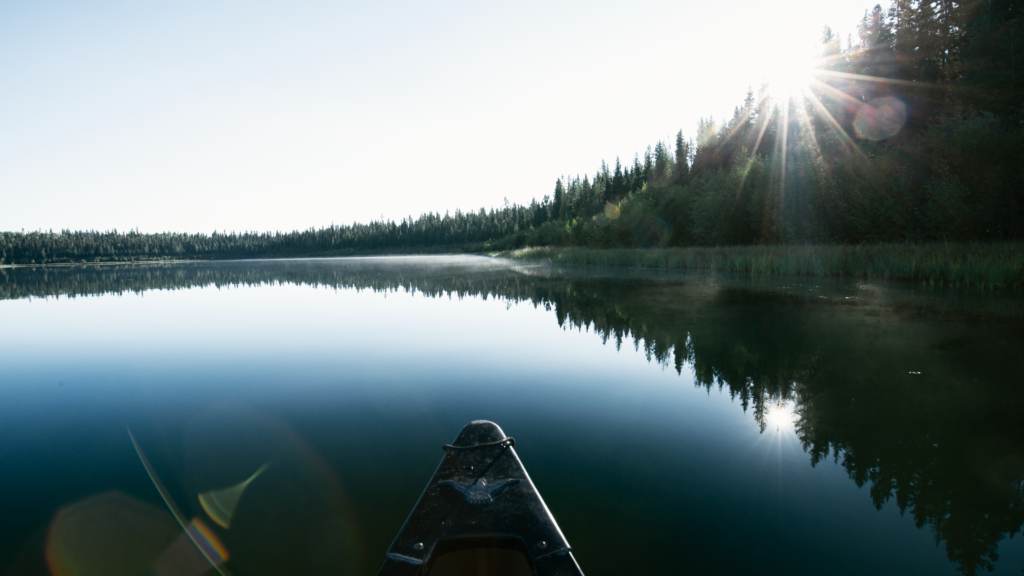 A canoe drifts on still lake while the sun shines on the water.