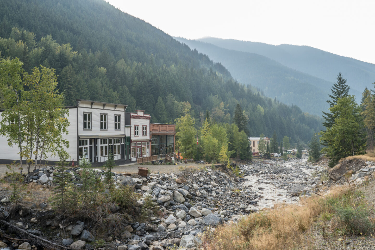 a rocky river runs in a valley past old wooden buildings